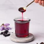 Homemade hibiscus syrup in a glass jar. A spoon is scooping some syrup.