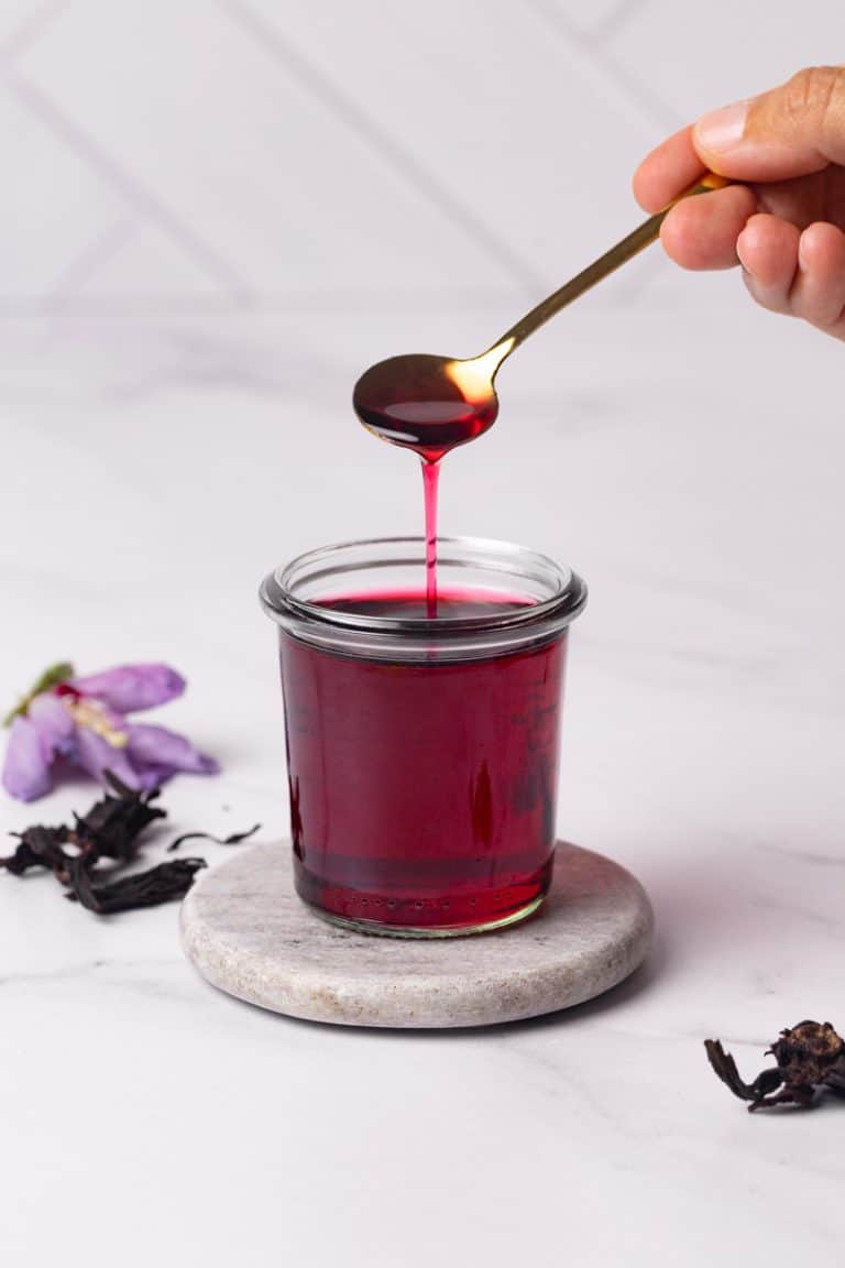 Homemade hibiscus syrup in a glass jar. A spoon is scooping some syrup.