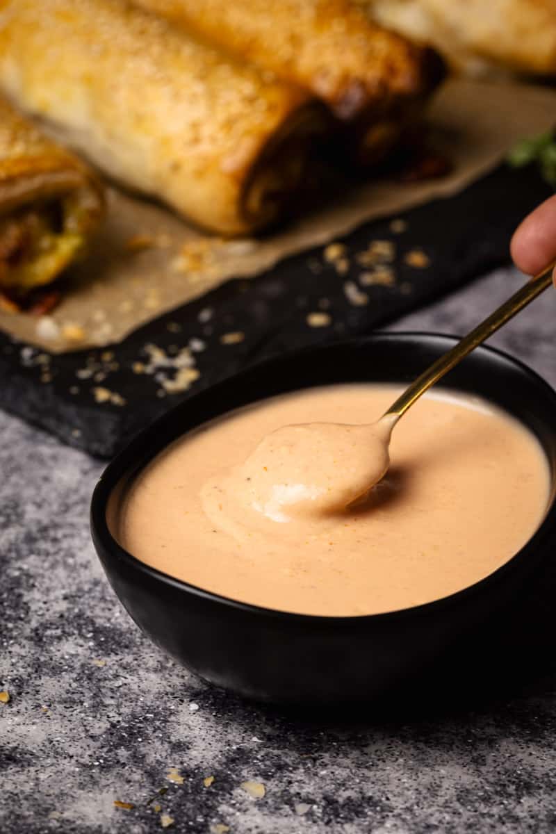 Hot dog sauce in a black bowl with a teaspoon scooping.