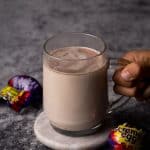 Cadbury creme egg hot chocolate in a glass cup next to creme eggs.