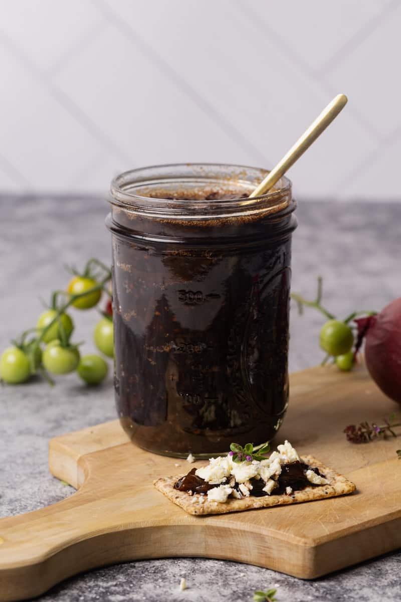 A glass jar filled with caramelized onion tomato jam on a wooden board.