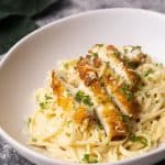 Breaded chicken on creamy linguine pasta in a white bowl next to green napkin.