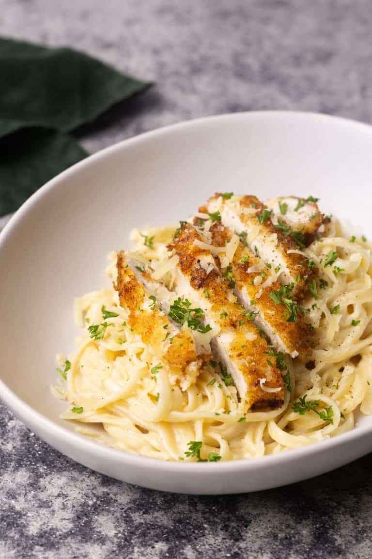 Breaded chicken on creamy linguine pasta in a white bowl next to green napkin.