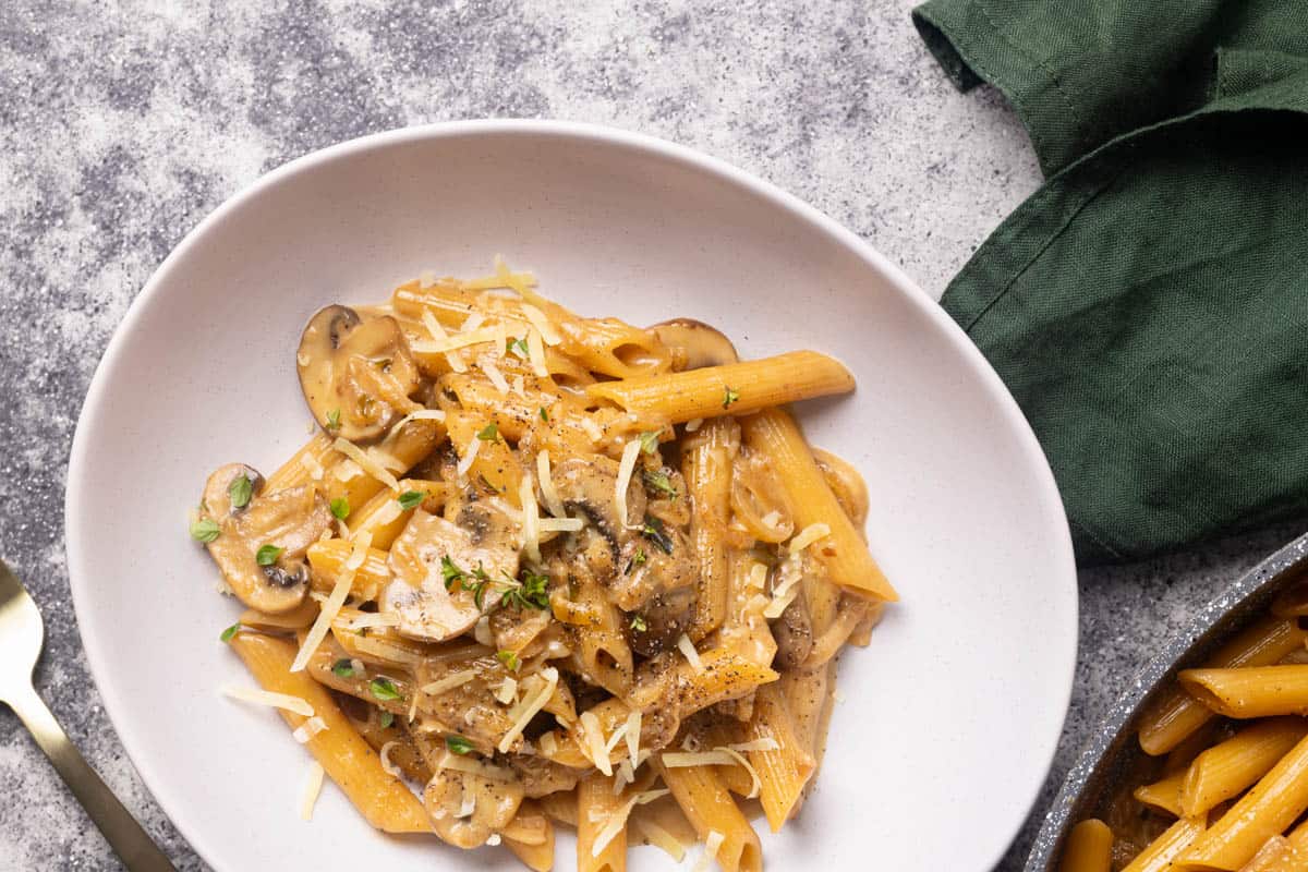 French onion pasta in a white bowl, next to a large pan and green napkin.