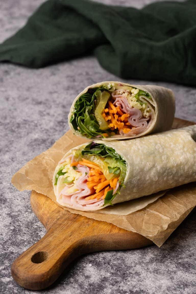 Ham and cheese wrap cut in half on a wooden board next to a green napkin.