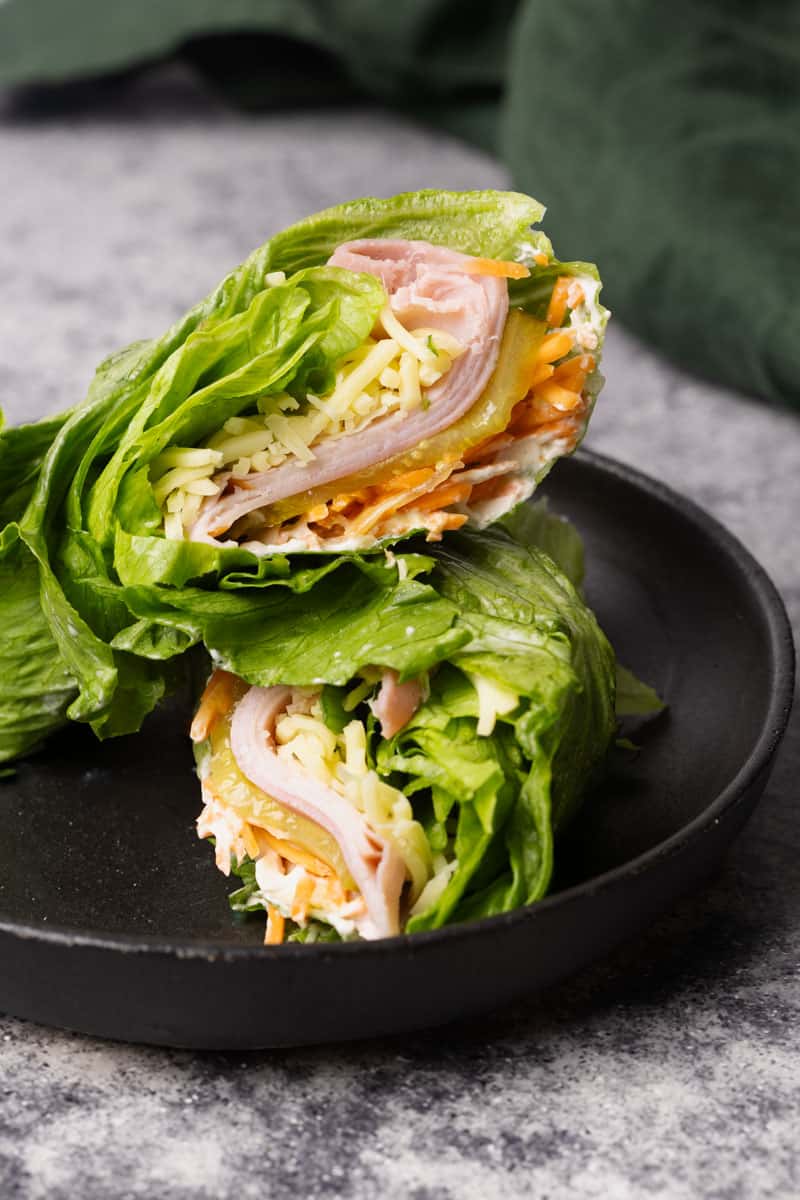 Ham and cheese lettuce wrap cut in half on a black plate next to a green napkin.
