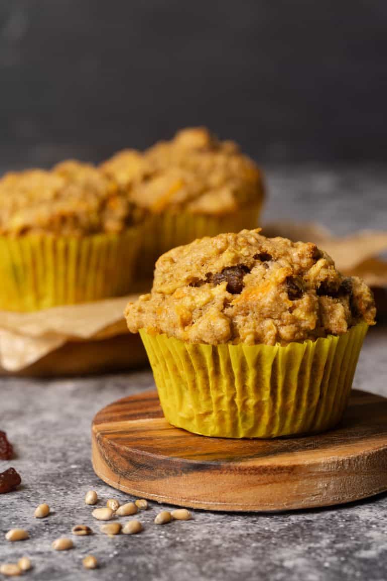 A muffin on a concrete bench next to two more muffins on a wooden cutting board. Moody light.