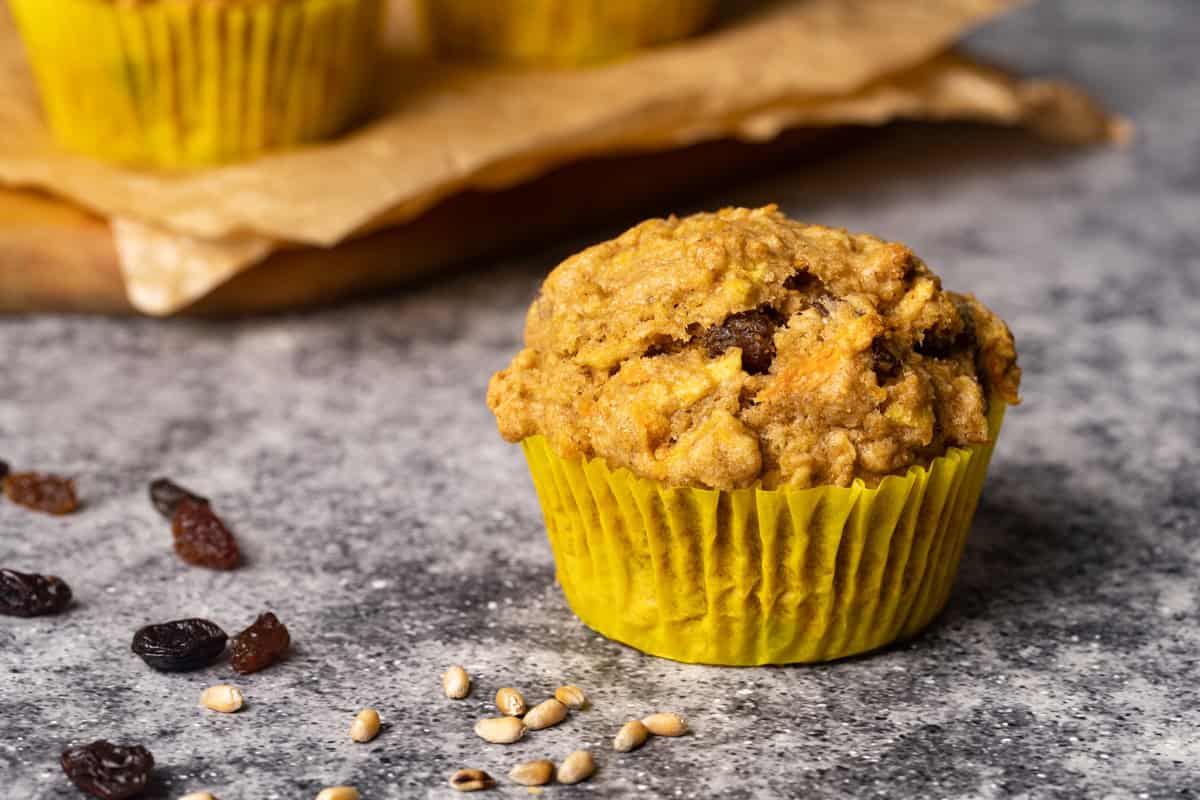 A muffin on a concrete bench next to two more muffins on a wooden cutting board. Moody light.