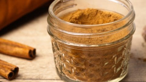 A jar of homemade Masala chai spice mix next to whole ingredients and a small spoon.