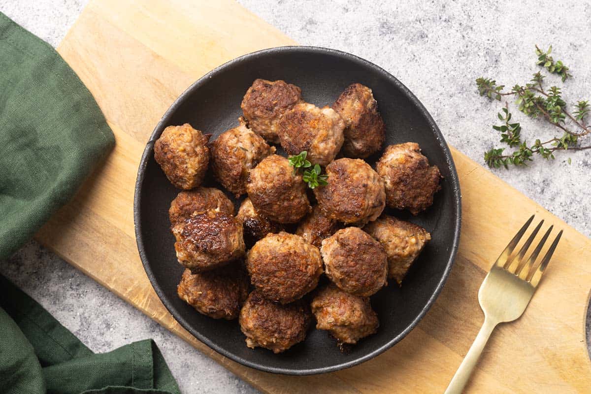 A black plate with lamb meatballs in a wooden board.