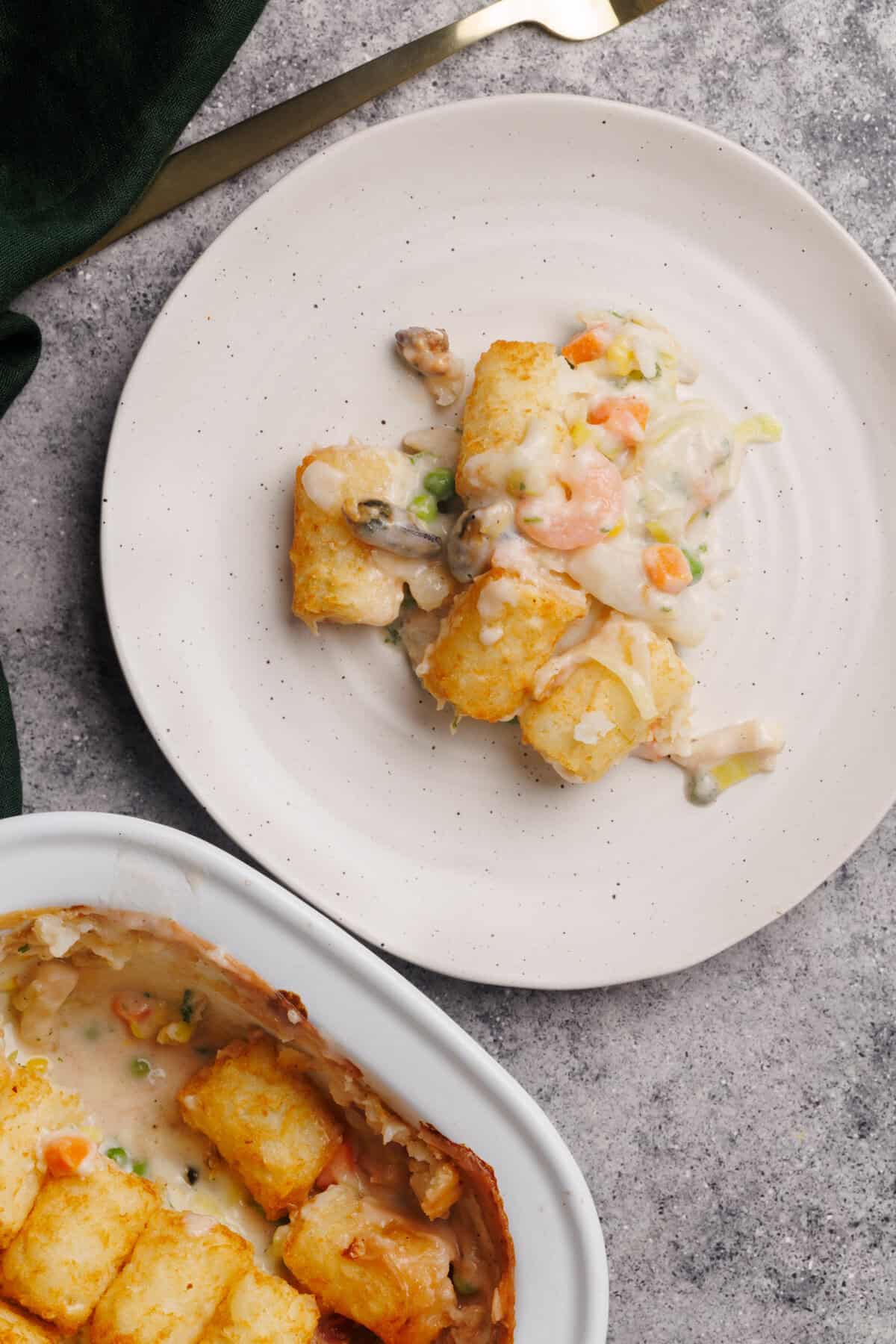 A serving of seafood pie on a white plate next to the casserole dish.