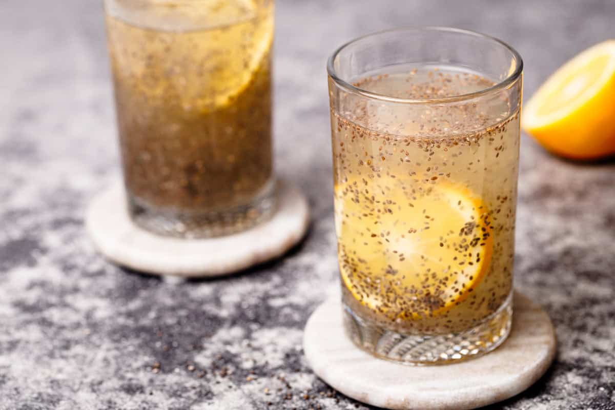 Two glasses with chia lemonade on marble coasters next to half a lemon.