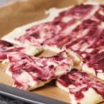 Frozen yogurt bark with berries on a baking sheet broken into pieces.