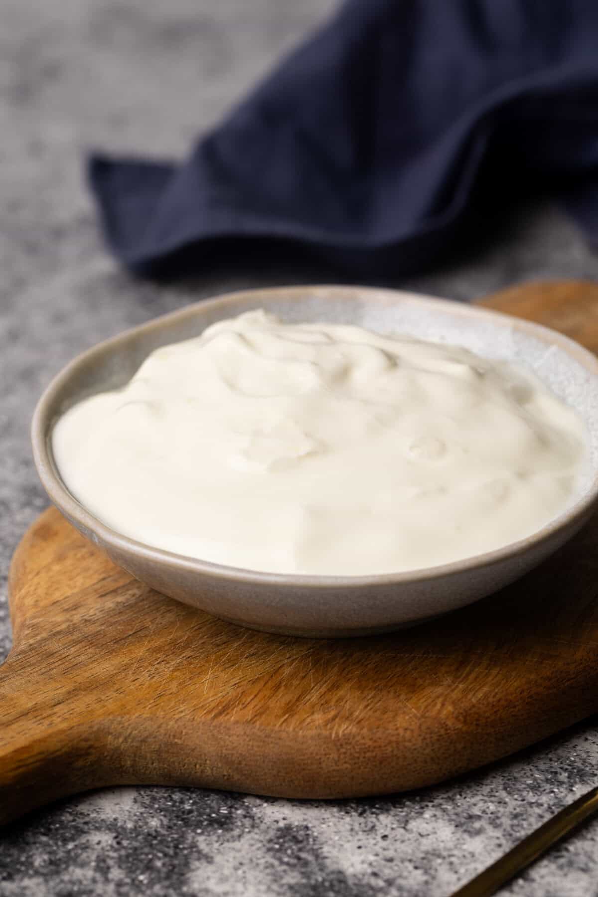 Yogurt in a small bowl on a wooden board.