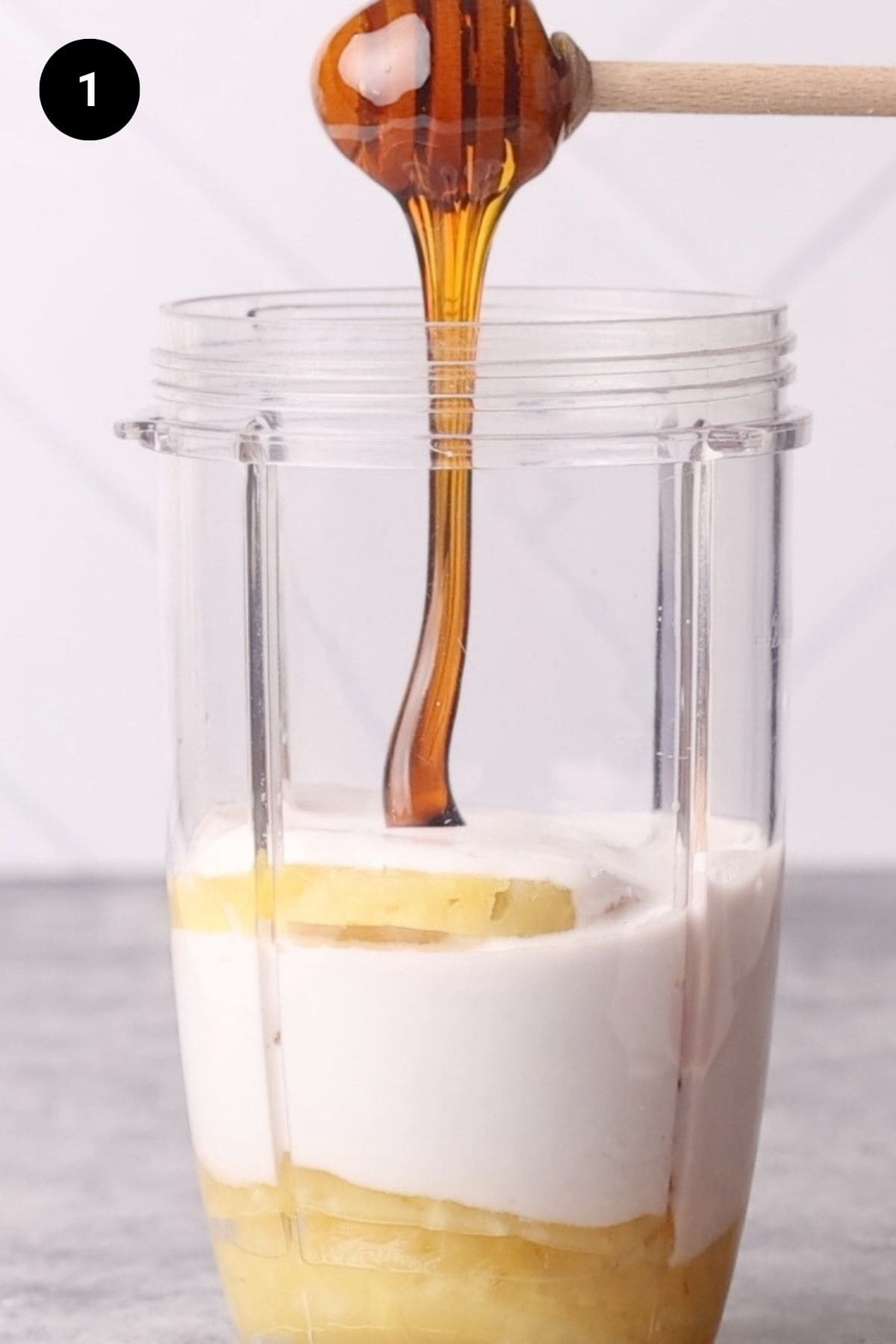 Honey being added to the coconut milk and pineapple slices in a blender.