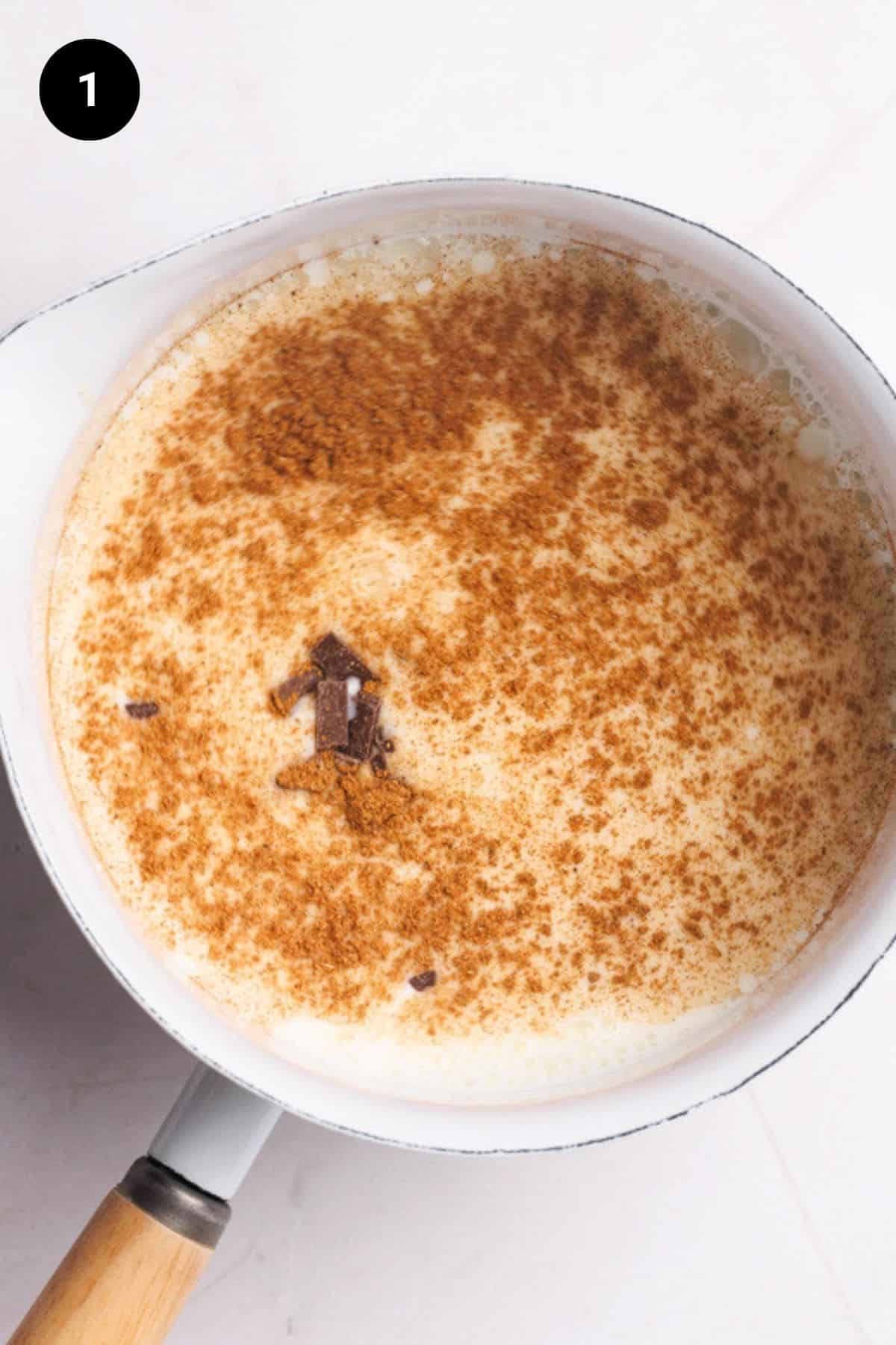 A white saucepan filled with milk, chocolate chips, and chai spices.