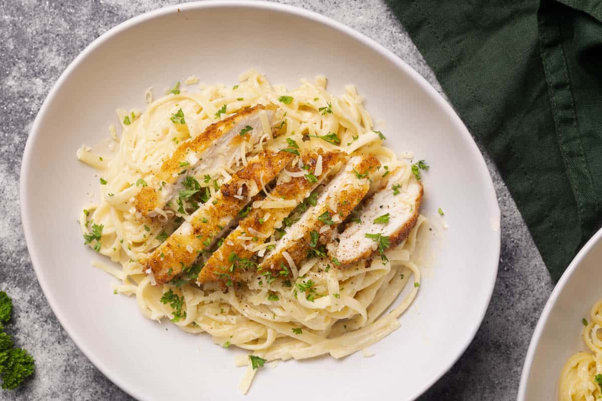 Chicken cutlets cut into strips on top of a creamy pasta dish.