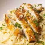 Crispy chicken breasts cut into strips on top of a creamy pasta dish.