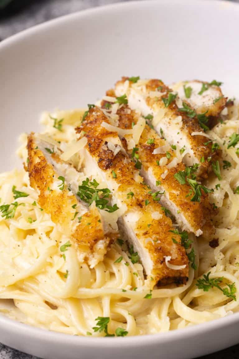 Crispy chicken breasts cut into strips on top of a creamy pasta dish.
