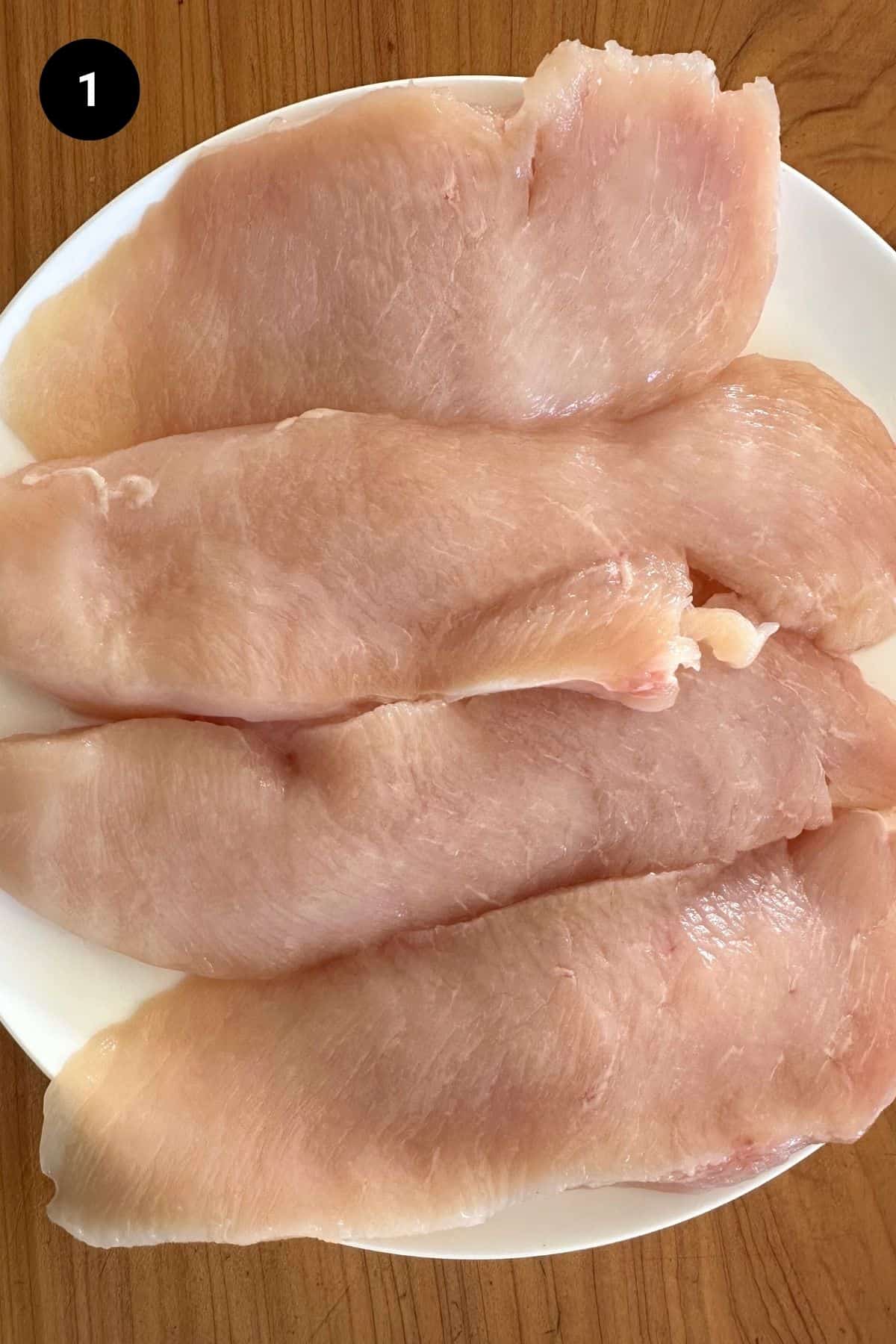 Raw chicken cutlets on a plate.