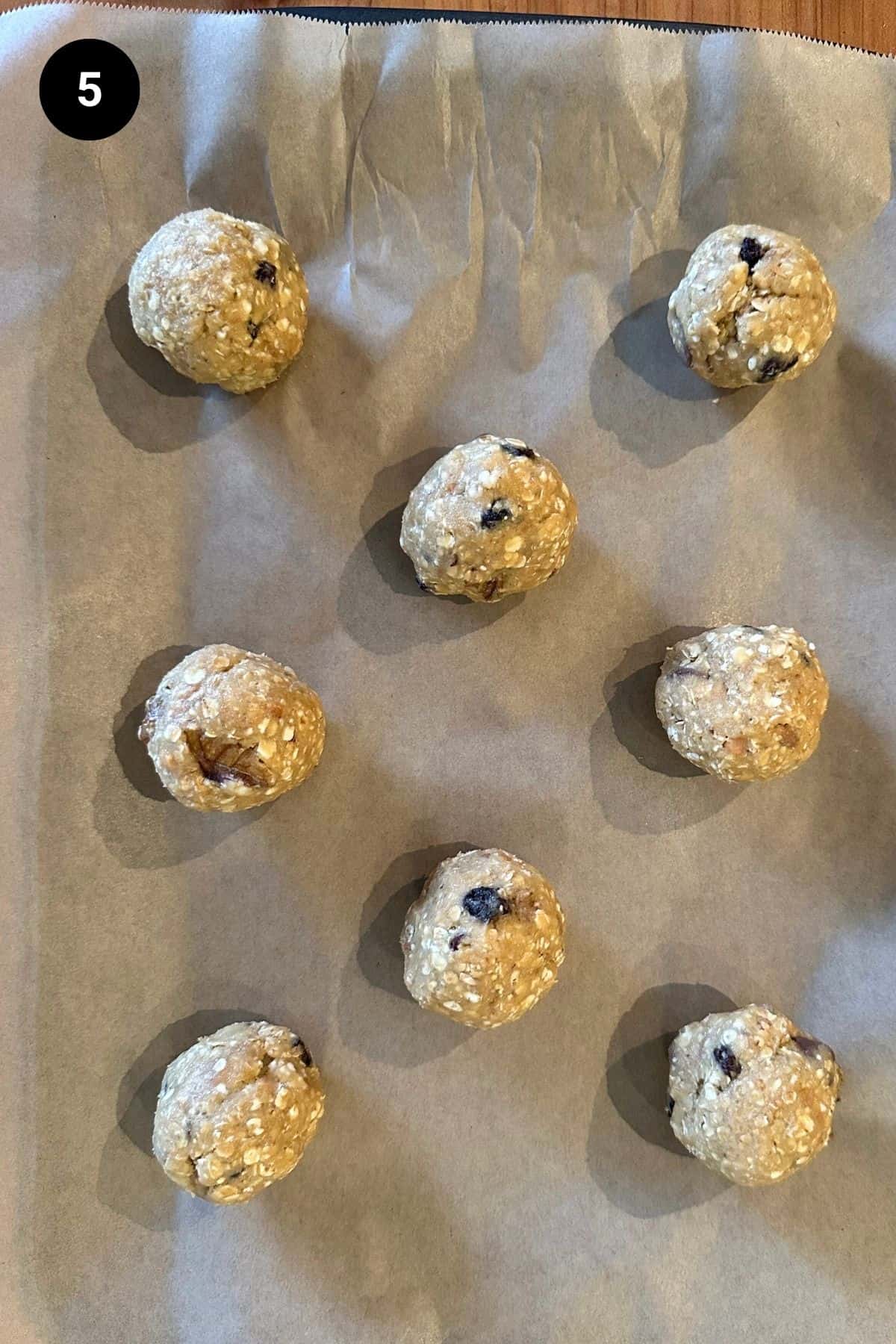 Raw cookie dough shaped into balls on a baking paper lined tray.