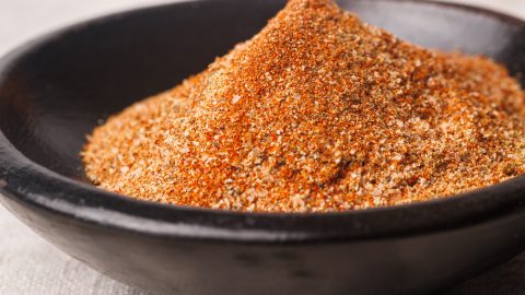 Lamb dry rub in a black bowl next to pepper kernels.