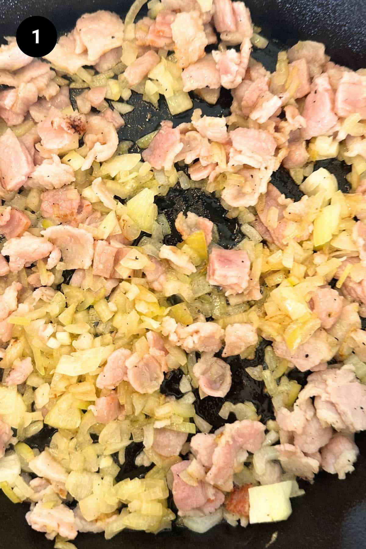 Onion and bacon being fried in a pan.