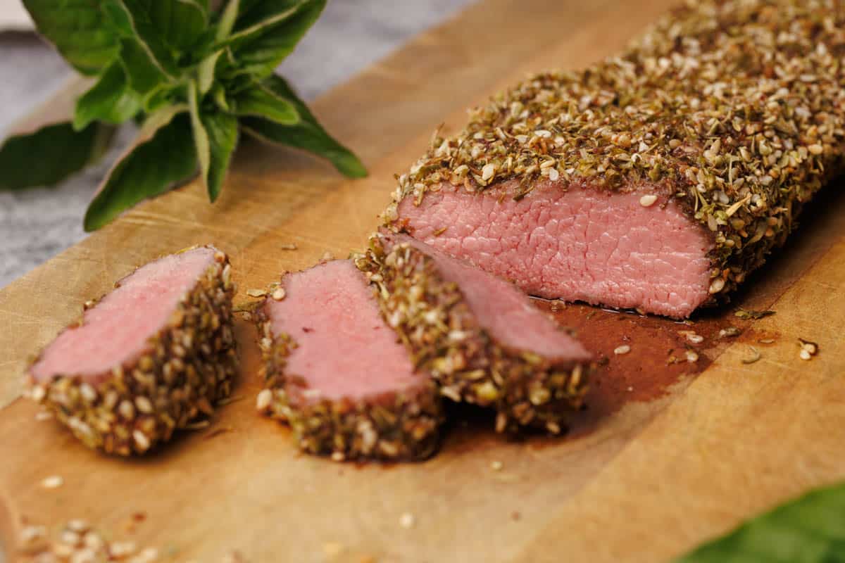 Za'atar crusted lamb loin cut up on a wooden board.