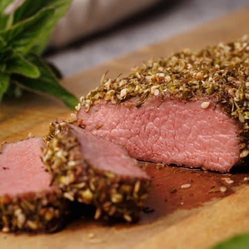 Za'atar crusted lamb loin cut up on a wooden board.