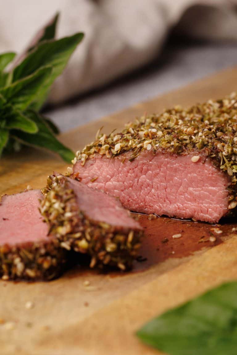 Za'atar crusted lamb loin cut up on a wooden board.