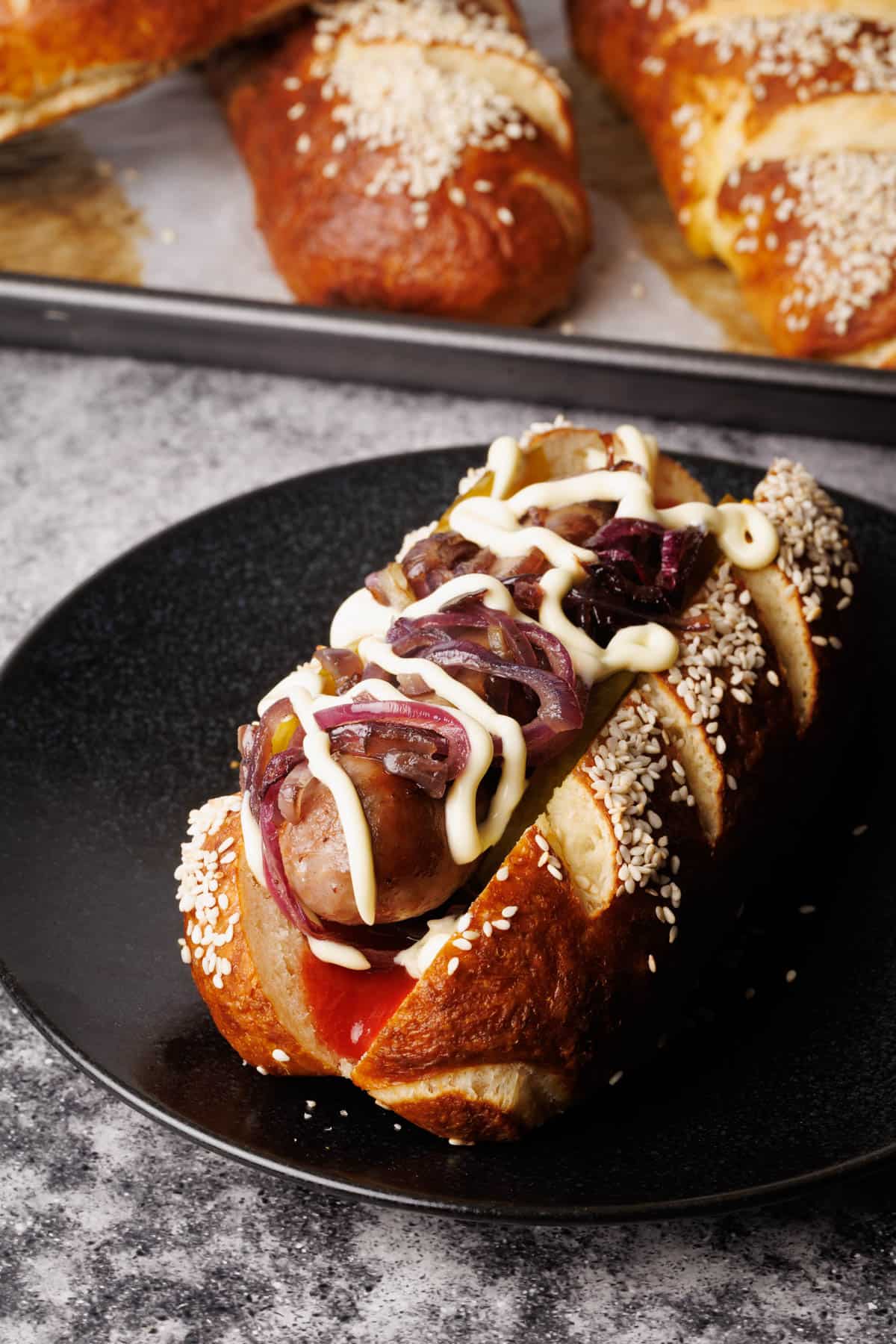 A pretzel hot dog on a black plate.