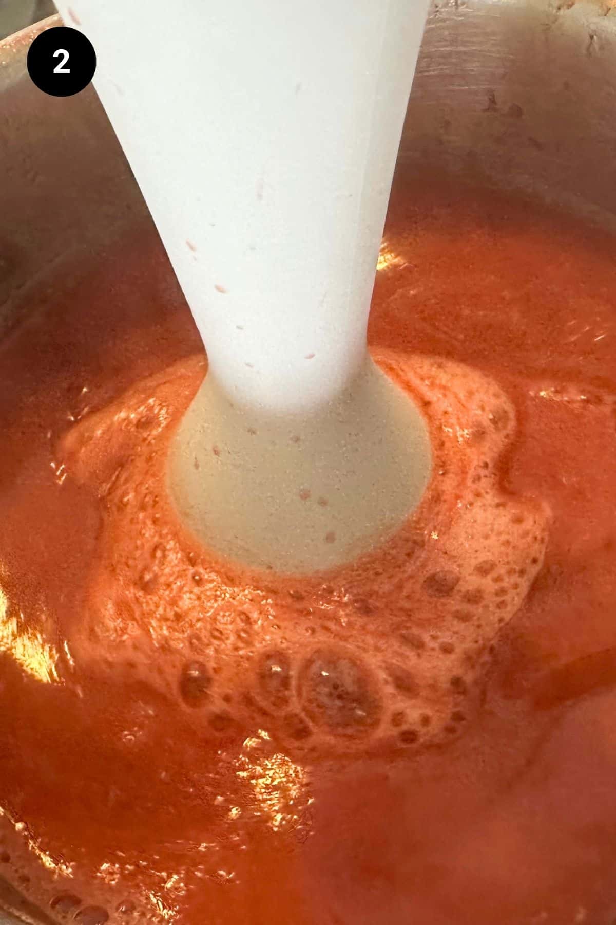 Strawberry puree being blended with an immersion blender.