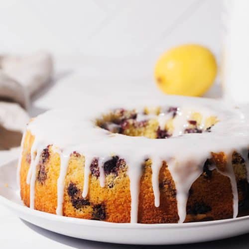 A pound cake in ring form on a white plate with white icing.