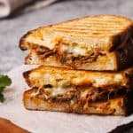 Grilled lamb sandwich cut in half on a wooden board.