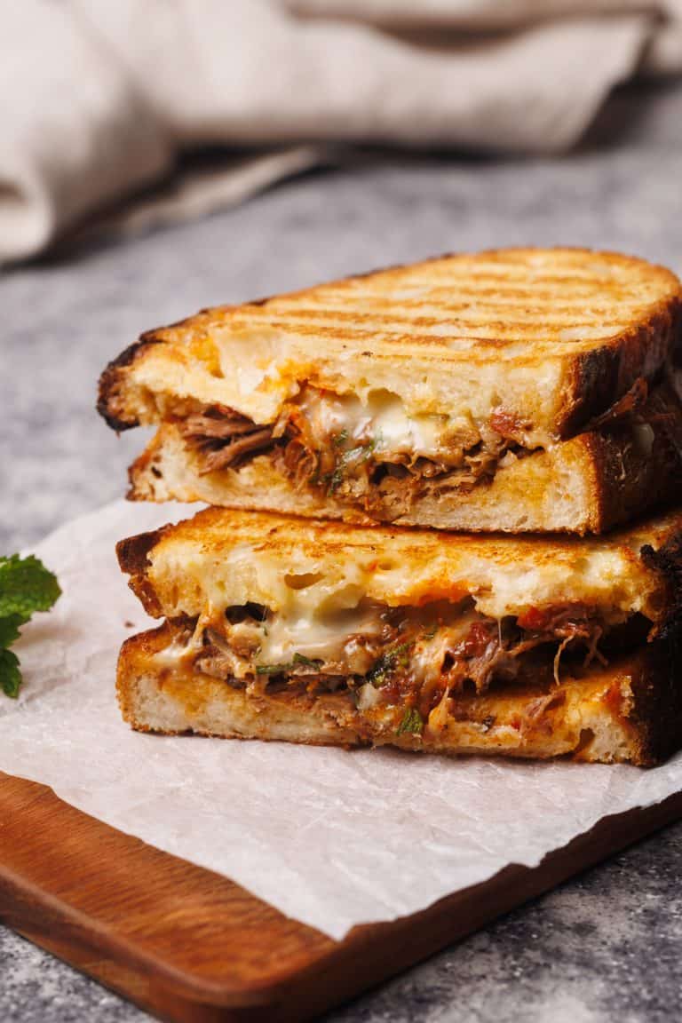 Grilled lamb sandwich cut in half on a wooden board.