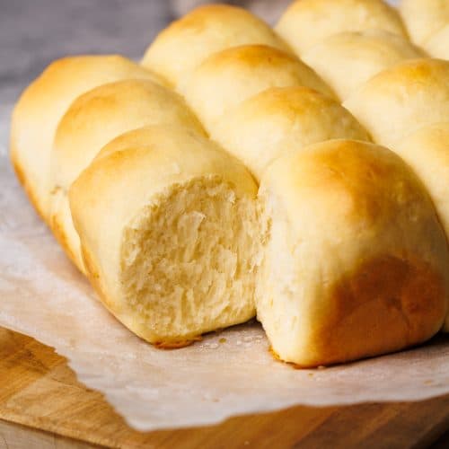 Dinner rolls on a parchment paper lined wooden board.