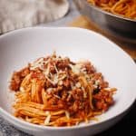 Lamb bolognese in a white bowl next to the large pan.