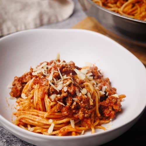 Lamb bolognese in a white bowl next to the large pan.