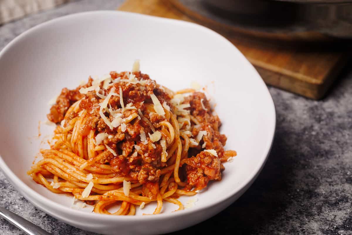 Lamb bolognese in a white bowl next to the large pan.