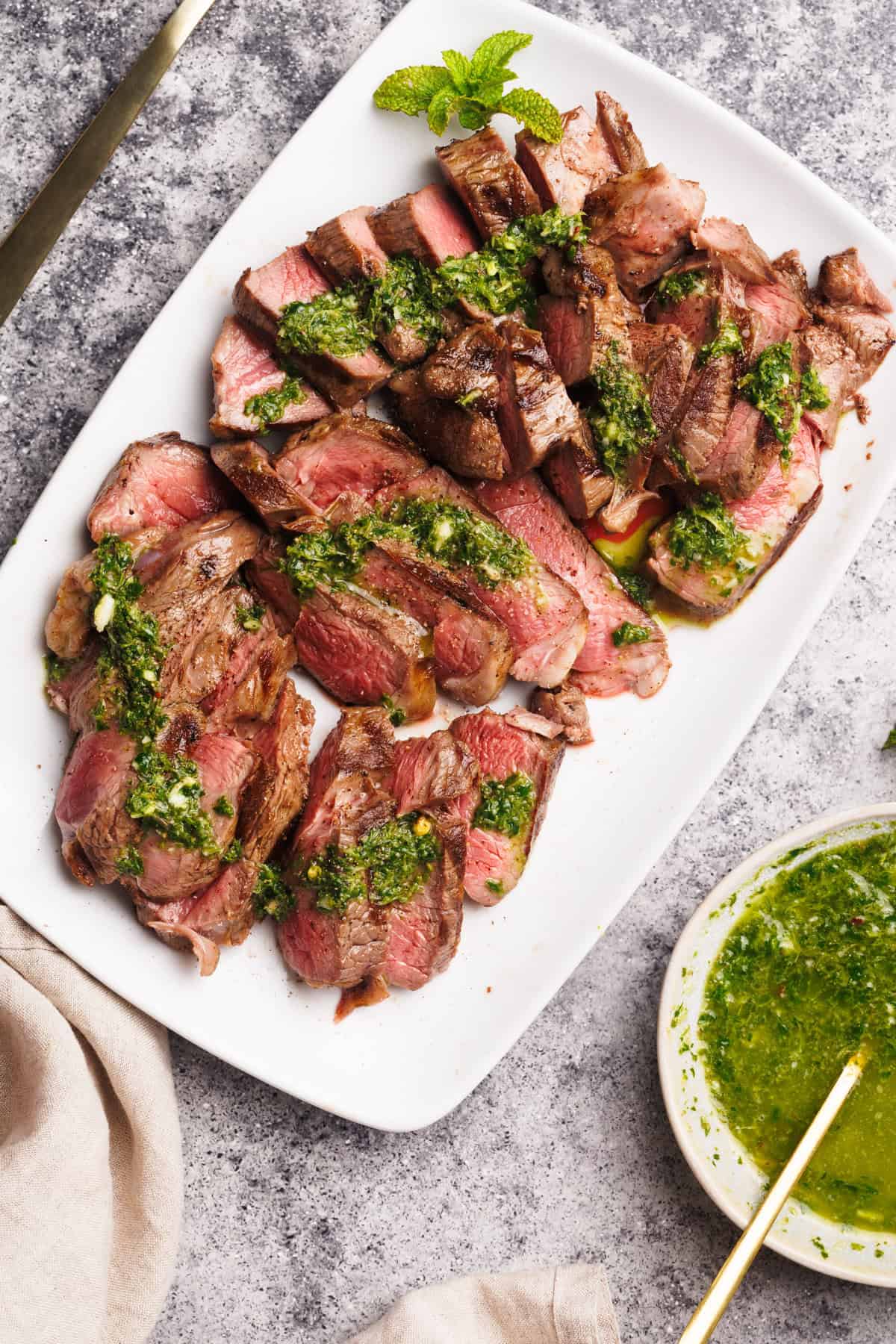 Steak pieces on a white serving plate with a mint sauce drizzled over.