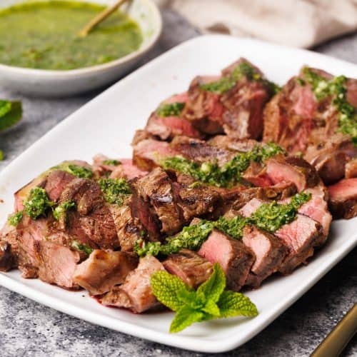 Steak pieces on a white serving plate with a mint sauce drizzled over.