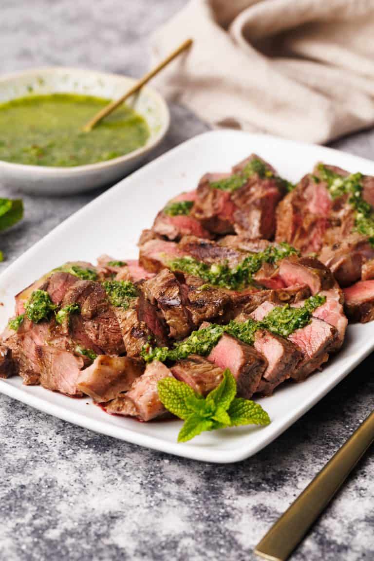 Steak pieces on a white serving plate with a mint sauce drizzled over.