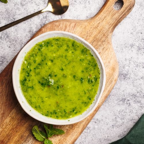 Mint chimichurri sauce in a small bowl on a wooden board.
