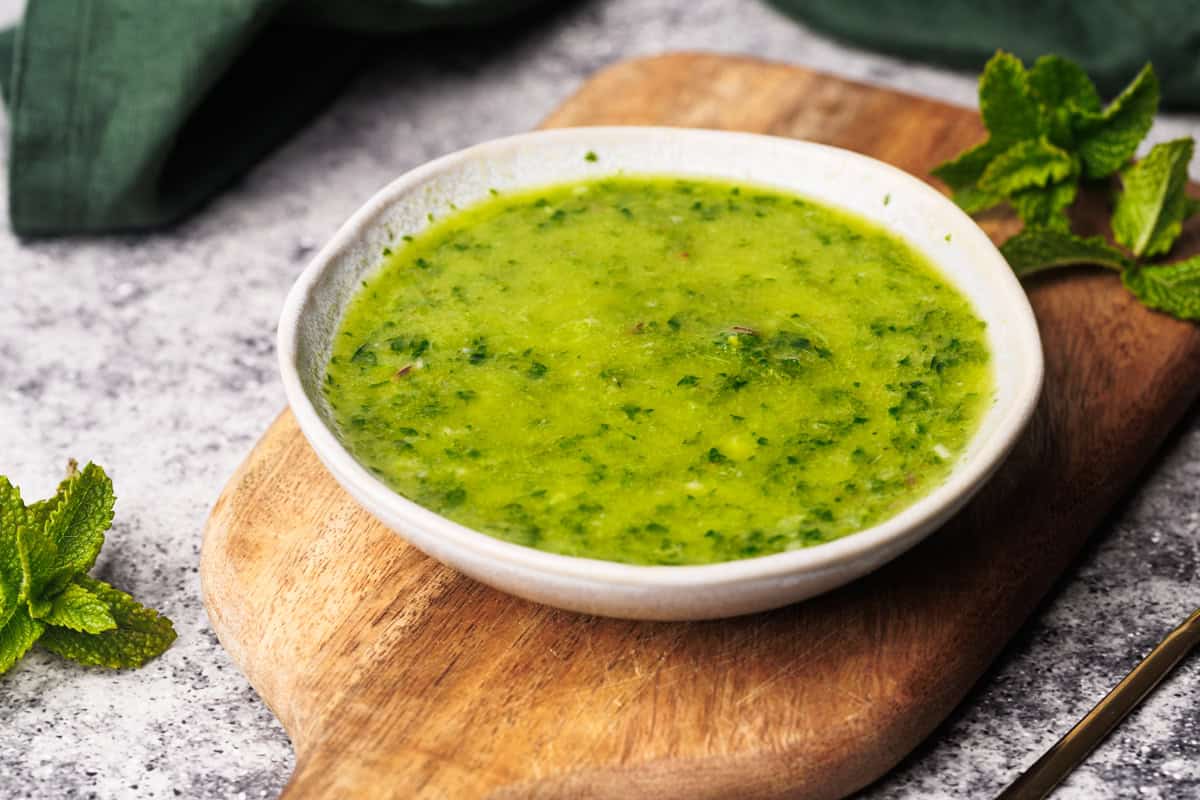 Mint chimichurri sauce in a small bowl on a wooden board.