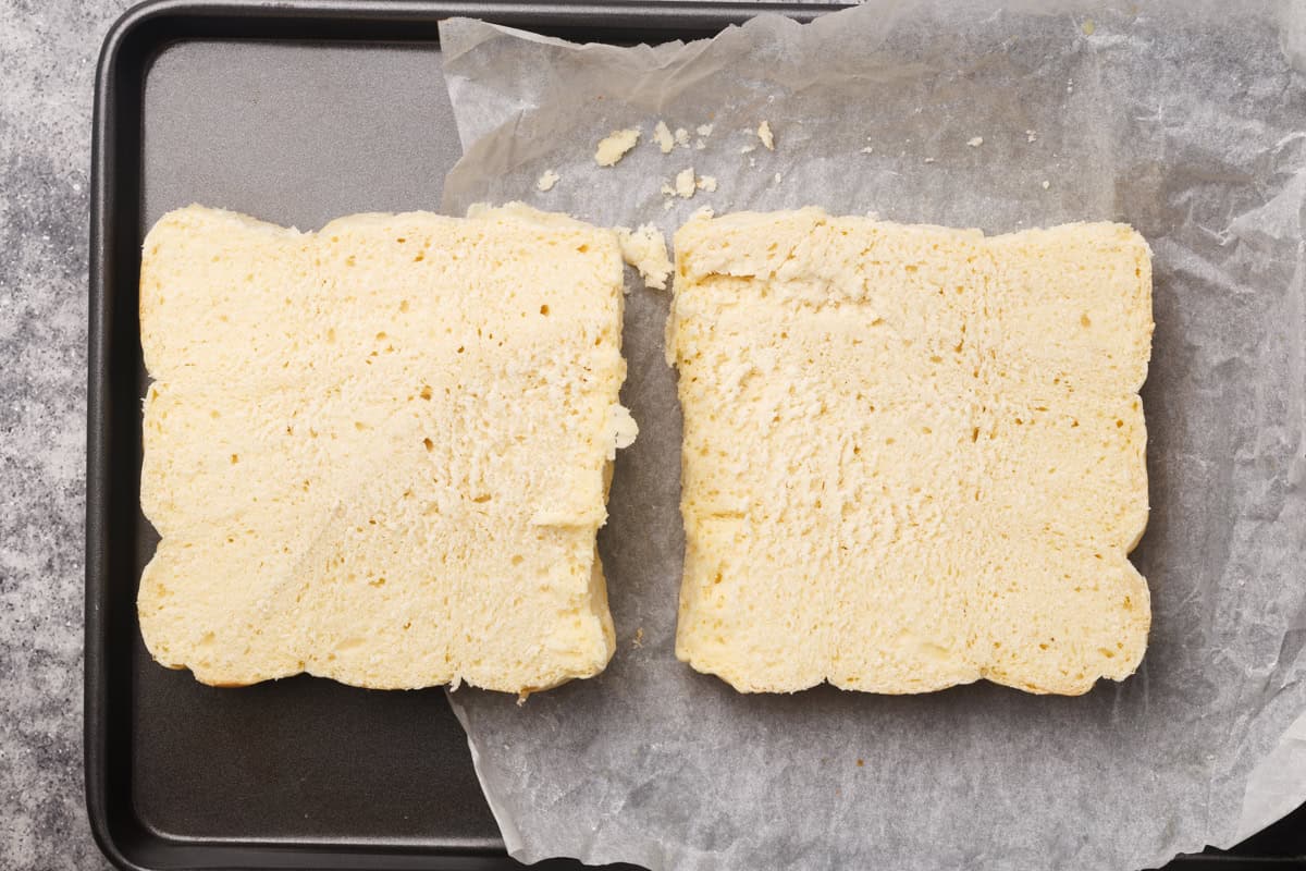 Slider buns cut in half on a lined baking tray.
