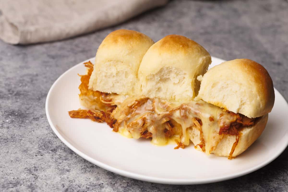 Pulled chicken sliders on a white plate next to linen tea towel.