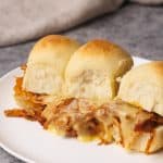 Pulled chicken sliders on a white plate next to linen tea towel.