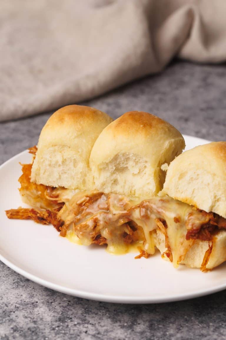 Pulled chicken sliders on a white plate next to linen tea towel.