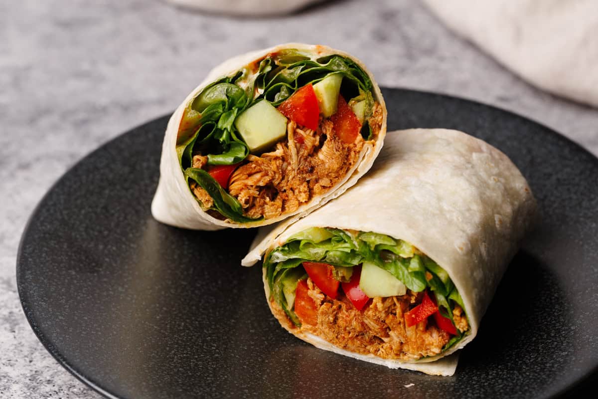 Chicken wrap cut in half on a black plate.