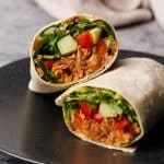 Chicken wrap cut in half on a black plate.